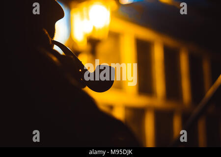 Uomo tubo di fumo durante la notte alla luce di una lanterna Foto Stock