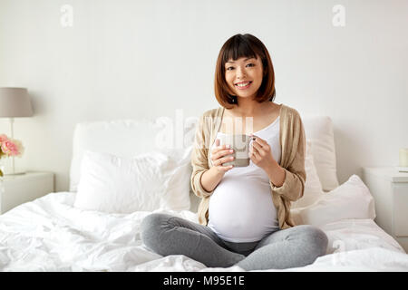 Felice donna incinta con tazza di bere il tè a casa Foto Stock