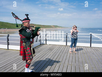 Scottish Piper in abito tradizionale su Saltburn il molo vittoriano. Saltburn dal mare, North Yorkshire, Inghilterra, Regno Unito. Foto Stock