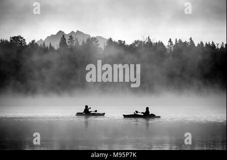 I pescatori in kayak alba sul lago Cassidy con la nebbia e la Cascade Mountain Range su alberi. Foto Stock