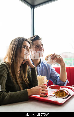 Un felice donna sorridente e un uomo bello stanno godendo i loro deliziosi e gustosi hamburger Foto Stock