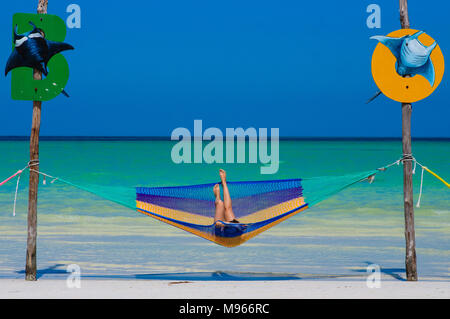 Donna rilassarsi in un'amaca su un acqua cristallina sul Mare dei Caraibi con cielo blu di Holbox, Messico Foto Stock