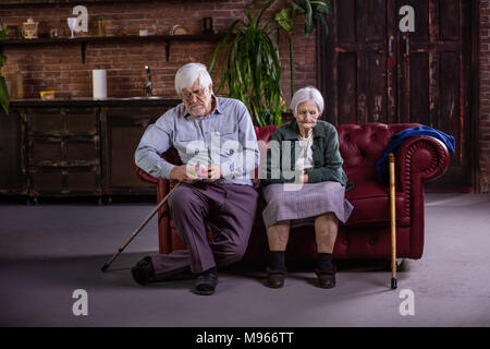 Coppia senior seduto sul divano. Matura in contenzioso e non di parlarsi. L'uomo gioca con puzzle, donna che guarda in basso con tristezza. Foto Stock