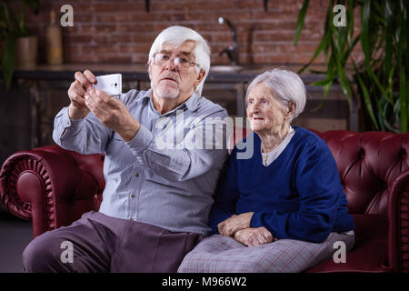 Coppia senior tenendo selfie su smart phone comodamente seduti sul divano di casa Foto Stock