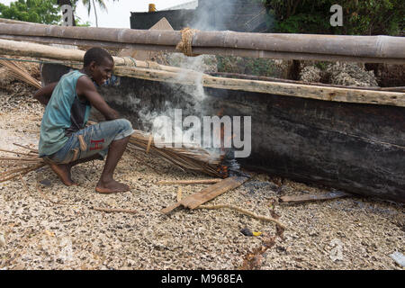 Un costruttore di barca con metodi tradizionali e la masterizzazione di un di legno scavato barca per sigillare e rendere a tenuta stagna sulla isola di Zanzibar Foto Stock