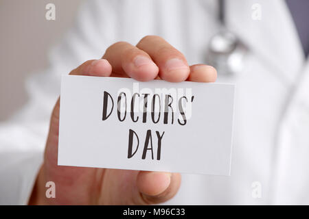 Primo piano di un giovane medico caucasica uomo, indossando il camice bianco, mostrando un cartello con scritto il testo medici giorno scritto in esso Foto Stock