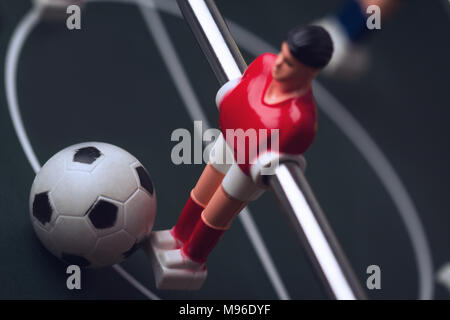 Primo piano orizzontale con il fuoco selettivo della maglietta rossa di figurine di giocatore con la palla ai suoi piedi sulla tabella di foosball soccer game Foto Stock