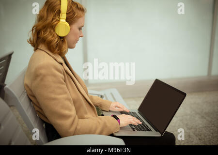 Giovane donna elenca la musica mentre si lavora sul computer portatile Foto Stock