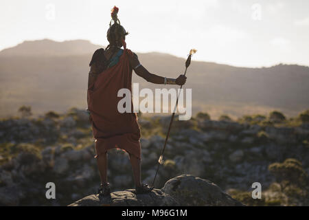 Vista posteriore del maasai uomo in piedi con bastone su roccia Foto Stock