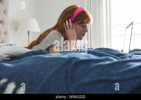 Donna con cuffie per ascoltare musica in camera da letto Foto Stock