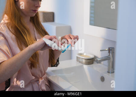 Donna applicando una pasta dentifricia su uno spazzolino da denti in bagno Foto Stock