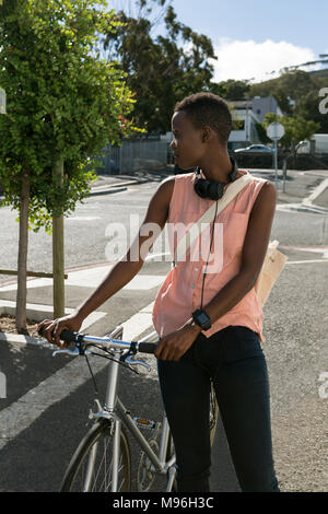 Donna in piedi con la bicicletta in una strada di città Foto Stock