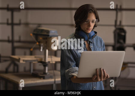 Saldatore femmina utilizzando laptop in officina Foto Stock