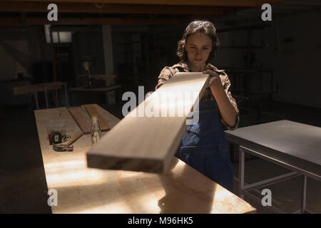 Saldatore femmina esaminando un pezzo di legno in officina Foto Stock
