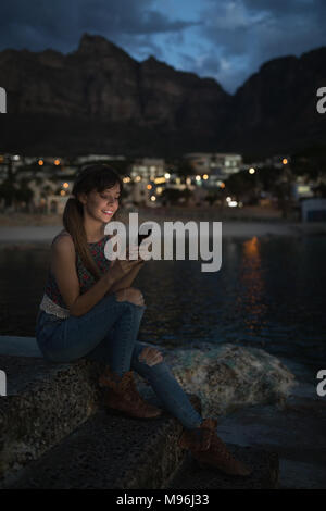 Donna che utilizza il telefono cellulare al rock pool Foto Stock