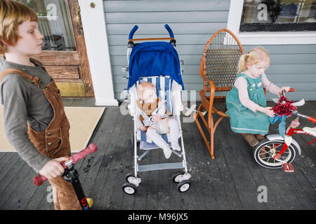 Ragazza con il triciclo accanto al bambino in blu la PRAM/passeggino Foto Stock