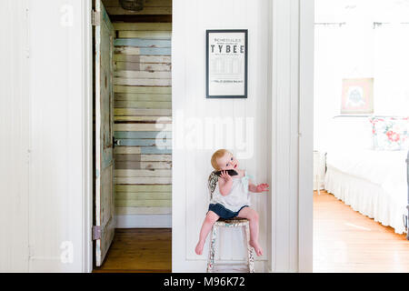 Baby su telefono seduti su una sedia Foto Stock