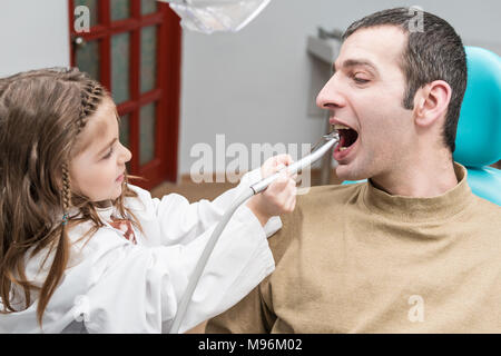 Bambina in una vestaglia di un dentista è denti di perforazione di un maschio adulto seduto in una sedia dentale Foto Stock