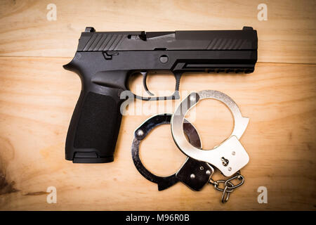 A pistola con bracciali a mano su una superficie di legno concept Foto Stock
