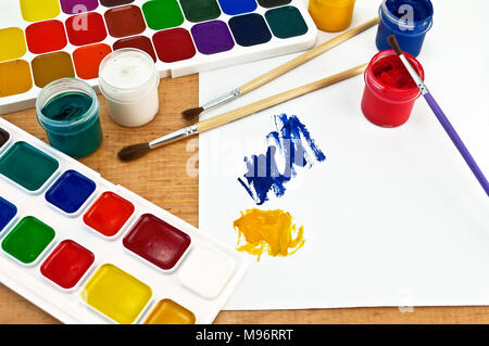 Due scatole di vernice, tre spazzole, vasi con gouache, un foglio di carta con un'immagine su una tavola di legno Foto Stock