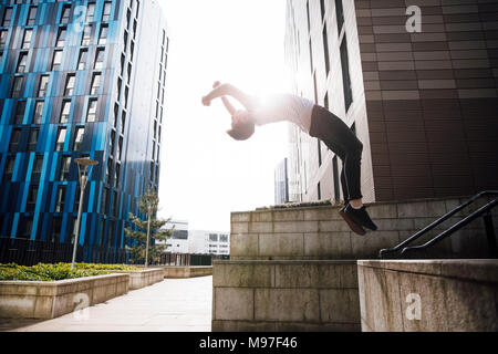 Freerunner sta facendo un backflip su un muro nella città. Foto Stock