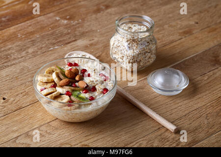 Composizione con vaschetta trasparente di fiocchi d'avena porrige con banana, kiwi, mandorla, pomergranate,asciugare i fiocchi d'avena in vetreria e cucchiaio di legno rustico woode Foto Stock
