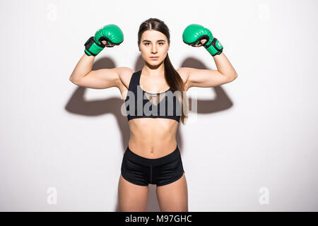 Sorridente brunette donna fitness in guantoni da pugilato mostrando il suo bicipite su sfondo bianco Foto Stock