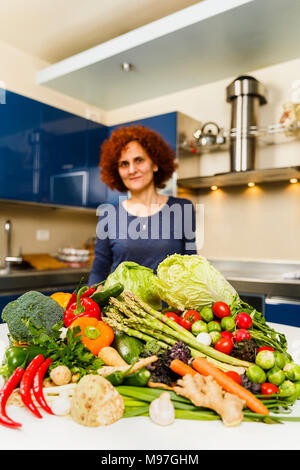 Donna cottura a casa, avente un grande mucchio di verdure su scheda Foto Stock