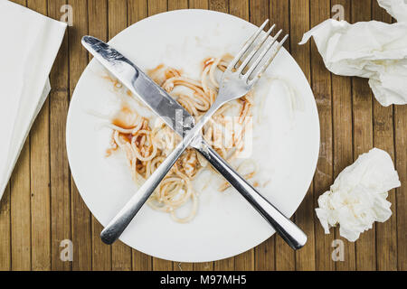 Resti di spaghetti, forchetta e coltello su una piastra bianca. I residui di cibo su una piastra al ristorante. Il completamento della cena. Foto Stock