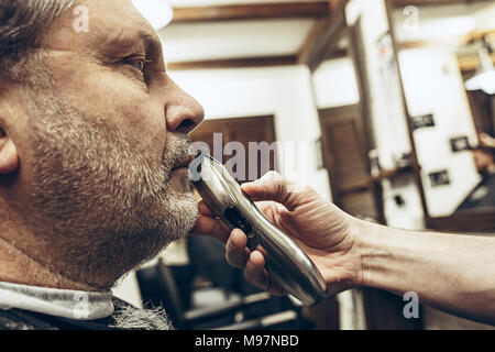 Close-up profilo laterale ritratto di bello senior barbuto uomo caucasico getting barba toelettatura in moderno barbiere. Parrucchiere Servizio client, makin Foto Stock