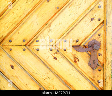 La sezione della vecchia gialla porta fatta di diagonal convergenti di tavole di legno con arrugginita leva maniglia di bloccaggio. Foto Stock