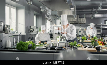 Famoso Chef lavora in un grande ristorante cucina con il suo aiuto. La cucina è piena di cibo, verdure e piatti di ebollizione. Egli sta cercando il gusto. Foto Stock