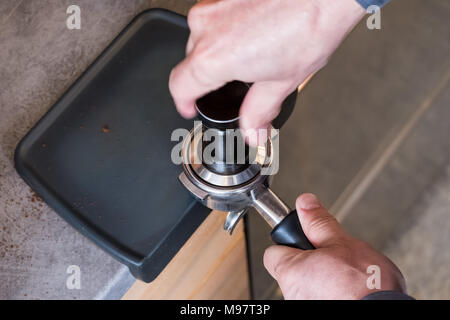 Barista premendo caffè appena macinato con dispositivo antimanomissione in portafilter per fare caffè espresso o cappuccino Foto Stock