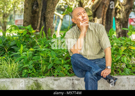 Veduta esterna del vecchio uomo si siede su un banco di lavoro, godendo la natura e avente un buon riposo. Tutti i problemi lasciati dietro Foto Stock