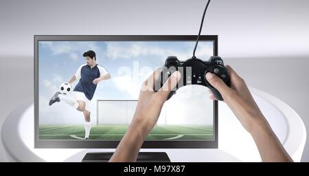 Mani che tengono il controller di gioco con il giocatore di calcio in televisione Foto Stock