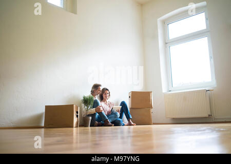 Coppia matura seduta sul pavimento nella stanza vuota accanto a scatole di cartone utilizzando tablet Foto Stock