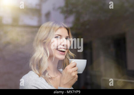 Ritratto di donna ridere con tazza di caffè dietro il vetro di finestra Foto Stock