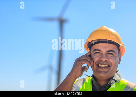 Ritratto di tecnico sorridente sul cellulare su una centrale eolica Foto Stock