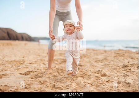 Madre aiutare piccola figlia di camminare sulla spiaggia