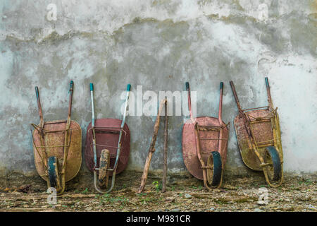 Quattro vecchie carriole appoggiata contro la parete Foto Stock