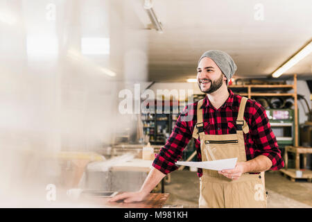 Felice lavoratore holding progetto in officina Foto Stock