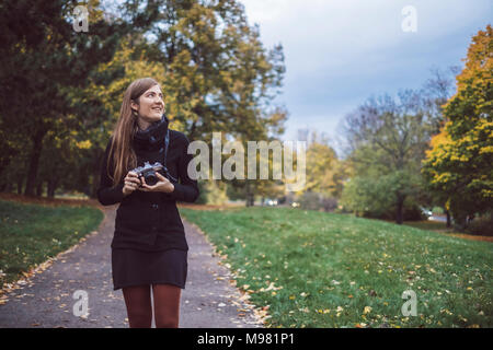 Giovane donna con fotocamera passeggiate nel parco autunnali Foto Stock