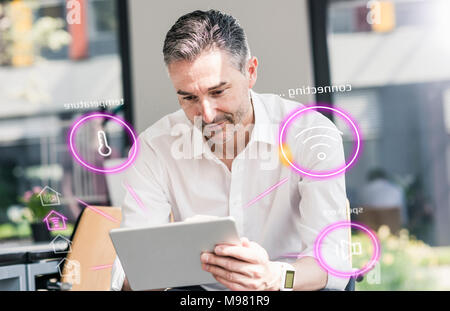Uomo seduto in ufficio utilizzando la tavoletta digitale per controllo remoto il suo smart home Foto Stock