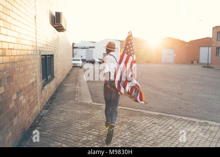 Vista posteriore del giovane uomo che corre con bandiera americana a retroilluminazione Foto Stock