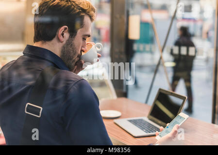 Giovane imprenditore in un cafe a stazione ferroviaria con un telefono cellulare di bere il caffè da cup Foto Stock