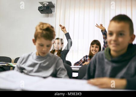 Gli studenti in classe con due ragazze ad alzare la mano Foto Stock