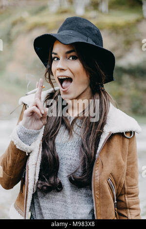Ritratto di felice giovane donna indossa flappy hat e fumare una sigaretta nella natura Foto Stock