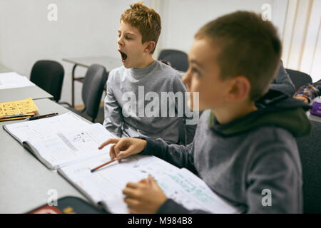 Gli studenti che studiano in classe con ragazzo sbadigli Foto Stock