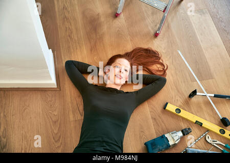 Redheaded donna sdraiata accanto a strumenti sul pavimento Foto Stock