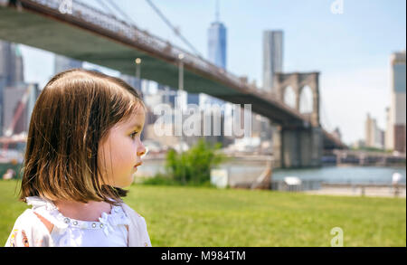 Stati Uniti d'America, New York, Brooklyn, Ritratto di bambina in park cercando da parte con il ponte di Brooklyn in background Foto Stock